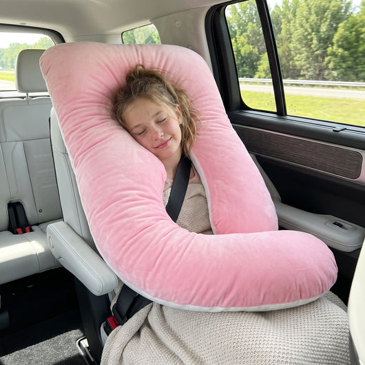 Girl asleep in the back seat with a pink Sleepy Miles pillow behind her