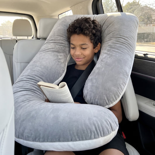 Boy reading in the back seat with a gray Sleepy Miles pillow